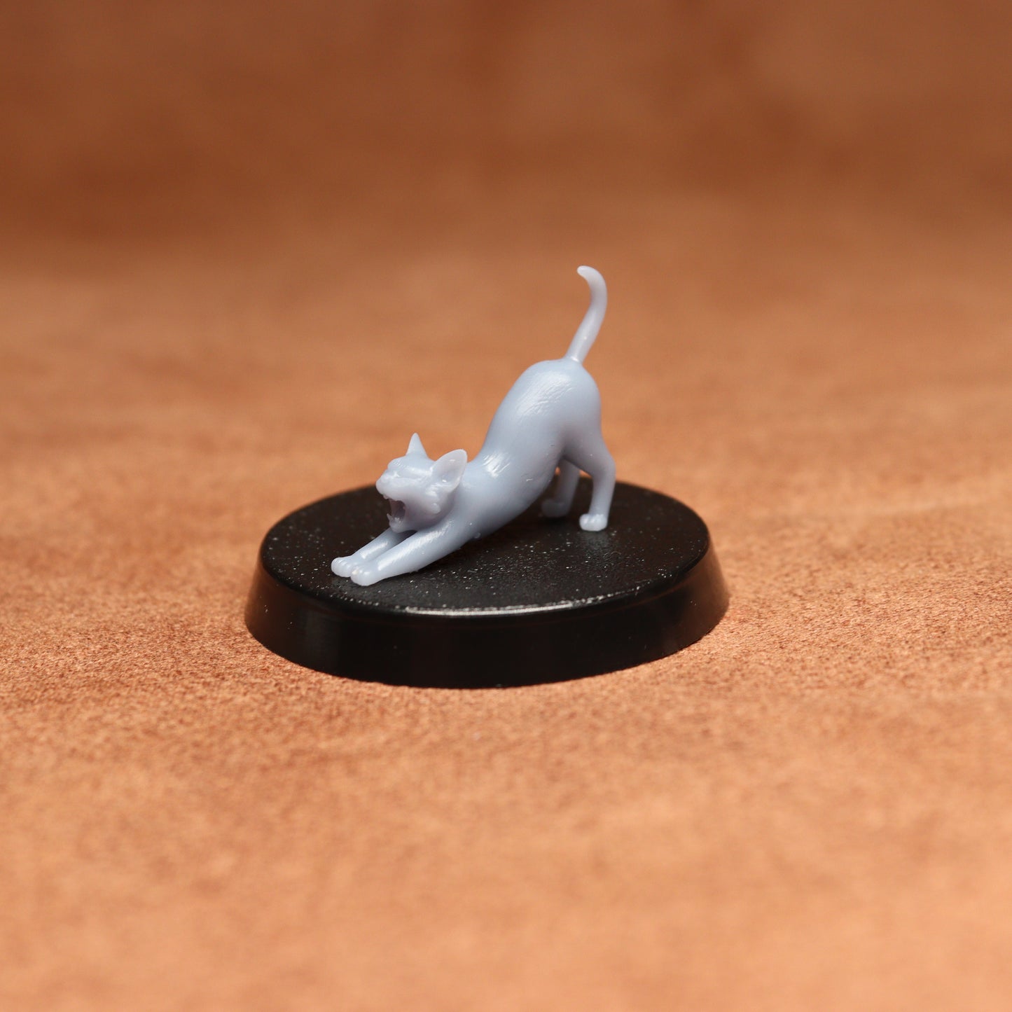 White cat figurine on a black round base against a brown background