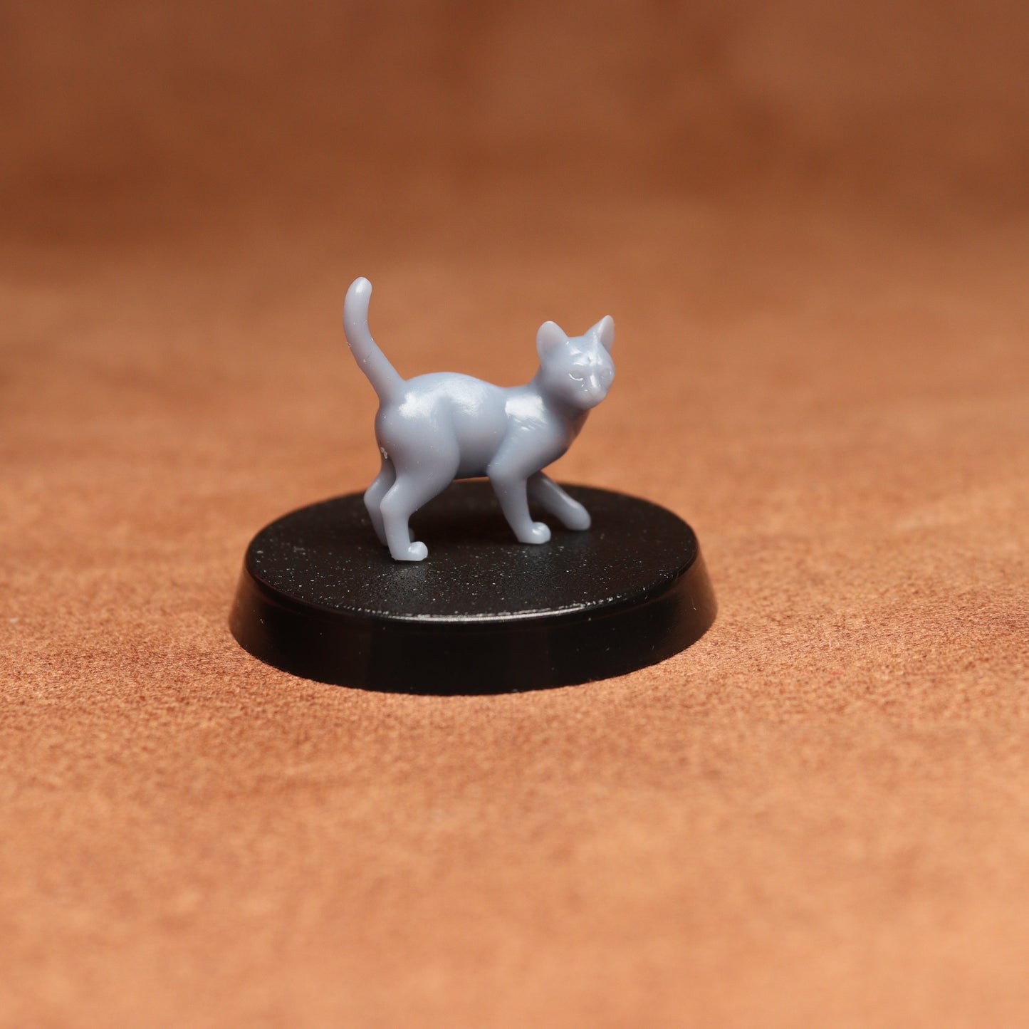 Small white cat figurine on a black round base against a brown background
