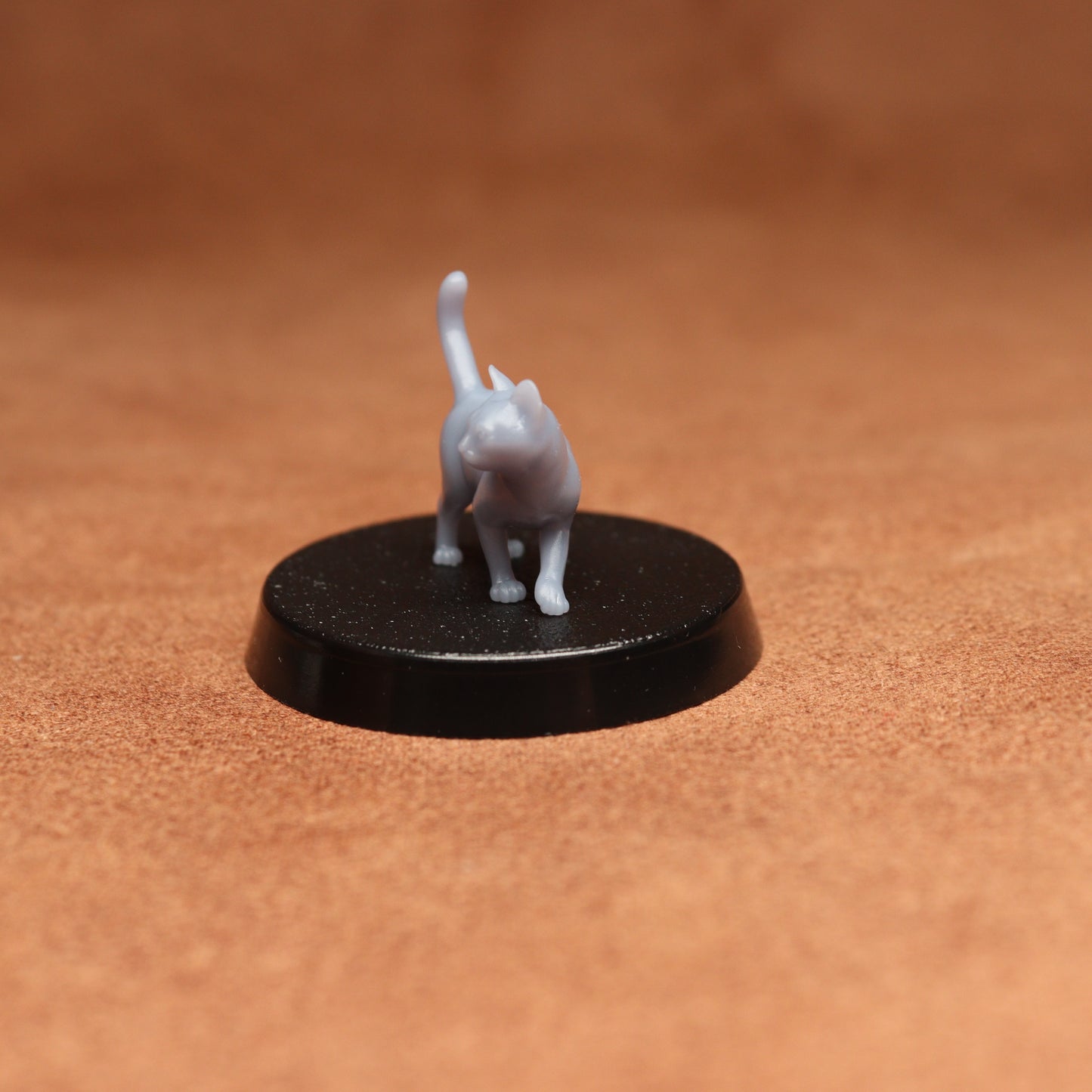 Small gray cat figurine on a black round base against a brown background