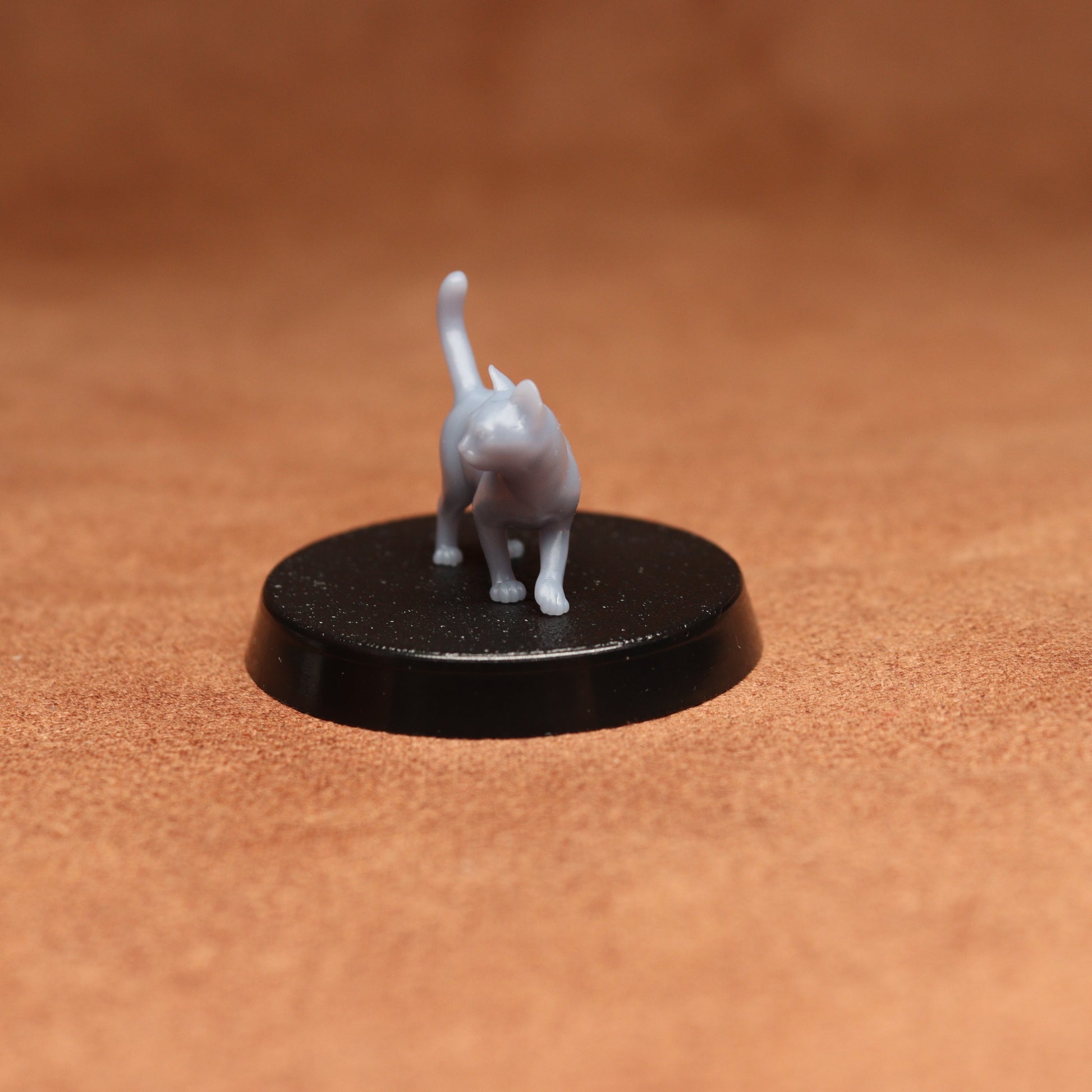 Small gray cat figurine on a black round base against a brown background