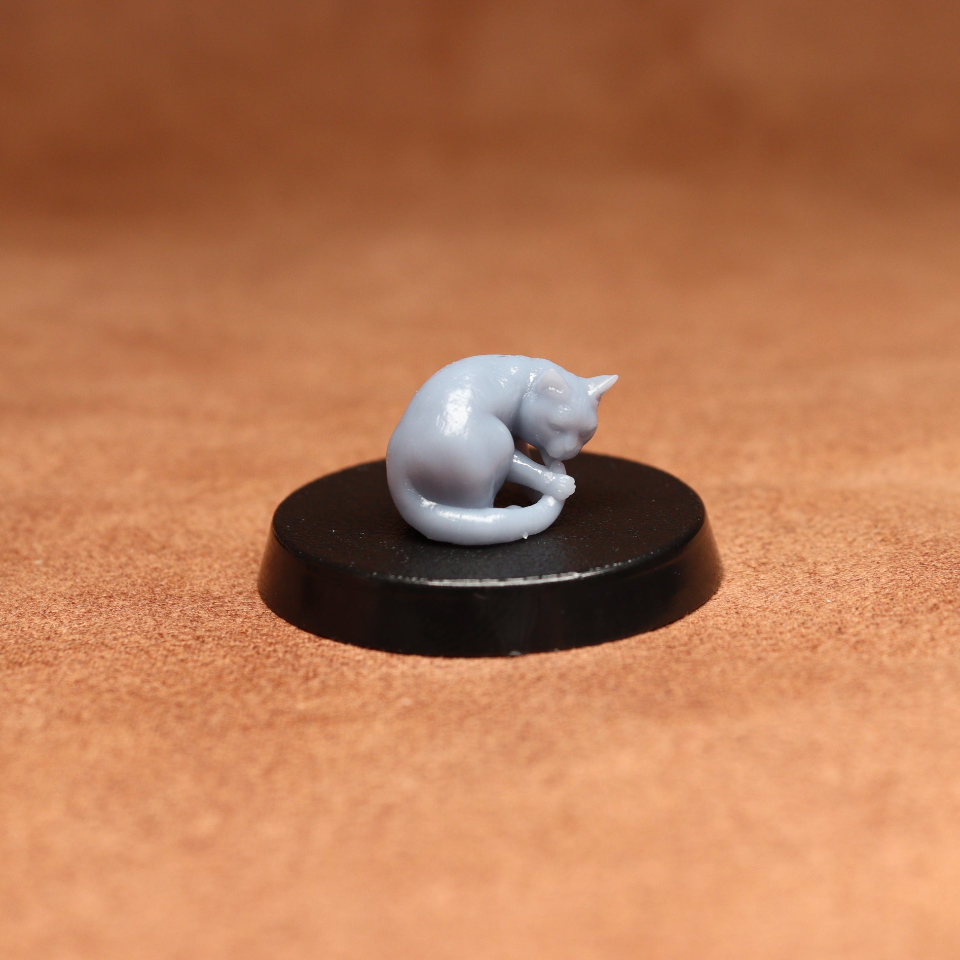 grey resin miniature cat figure on a black base with a brown background