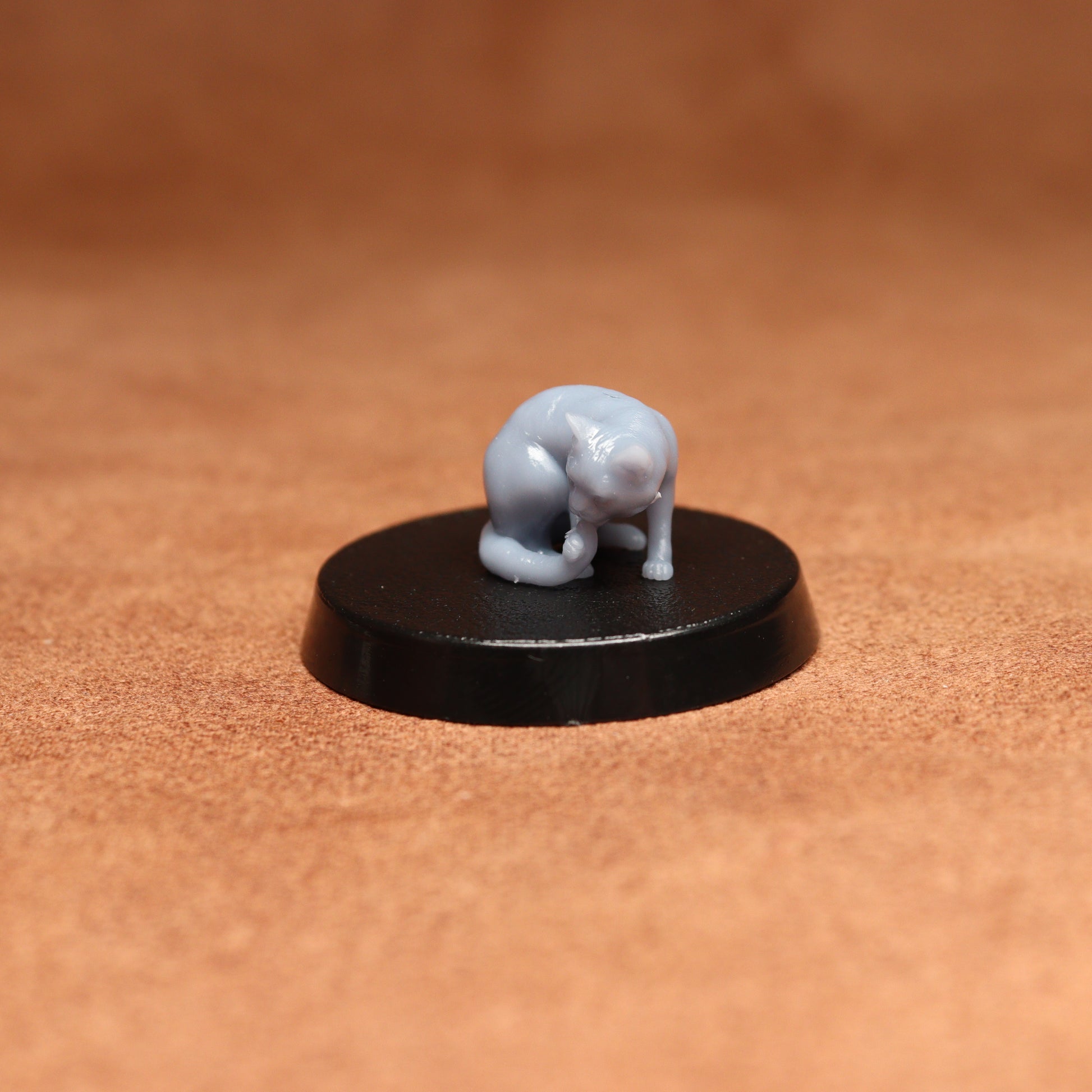 grey resin miniature cat figure on a black base with a brown background