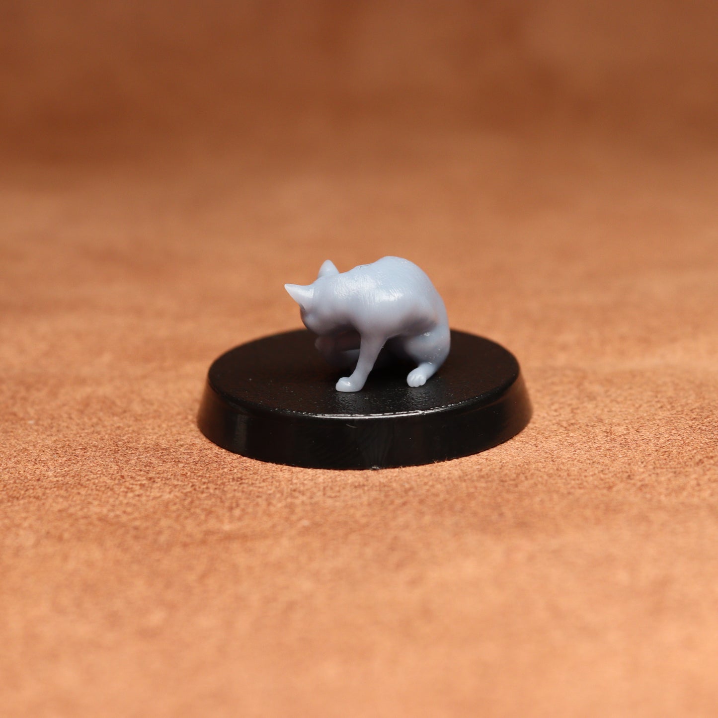 grey resin miniature cat figure on a black base with a brown background