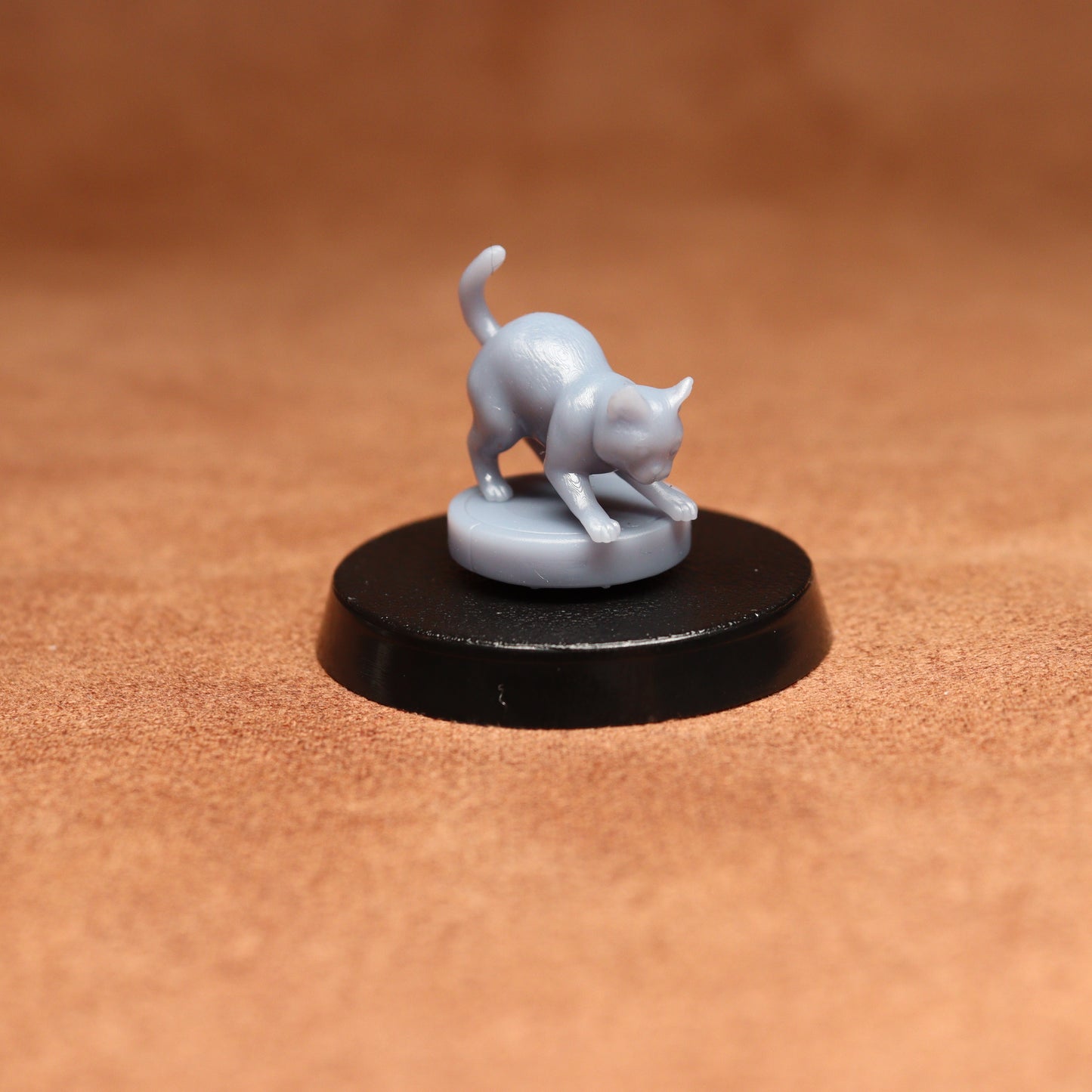 grey resin miniature cat figure on a black base with a brown background