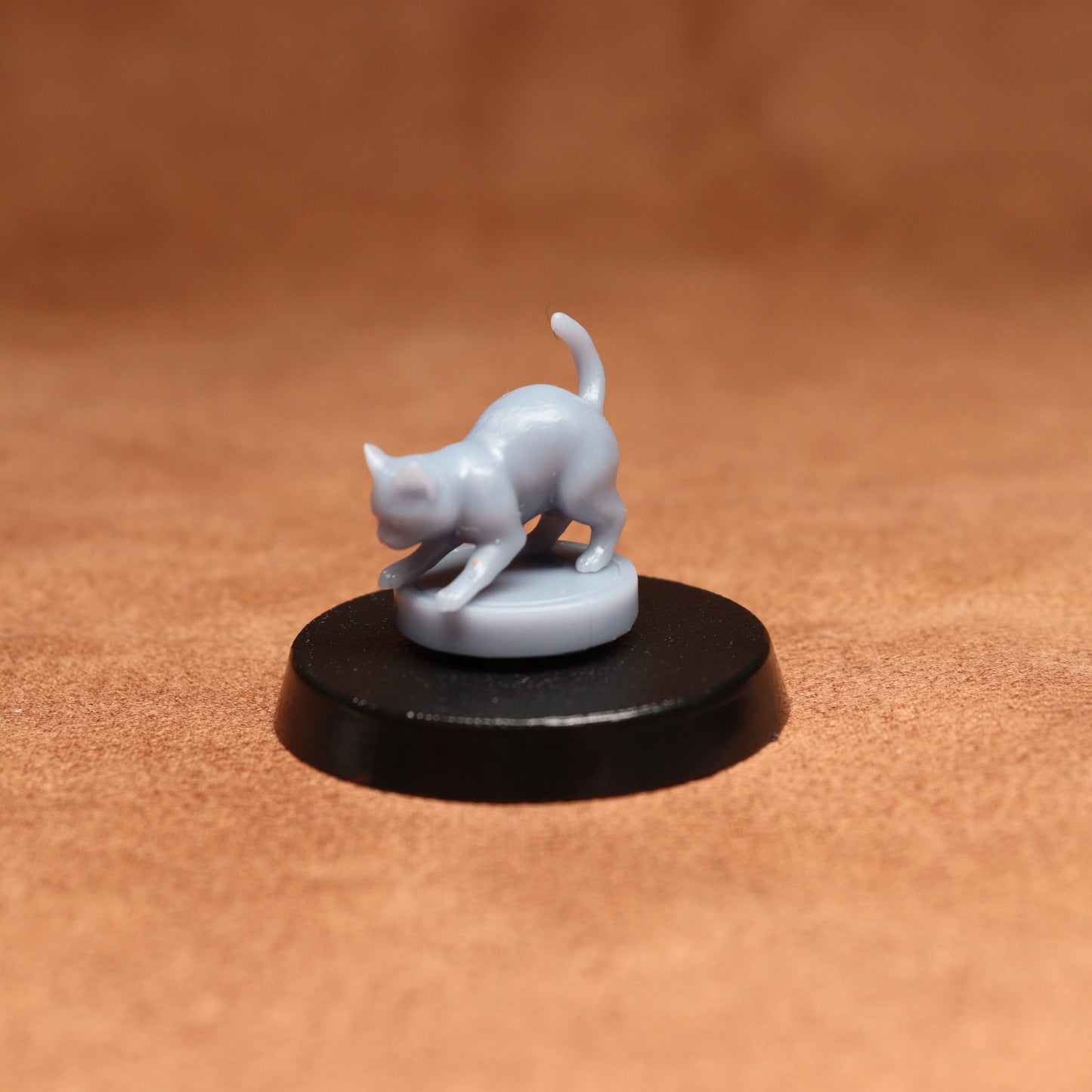 grey resin miniature cat figure on a black base with a brown background