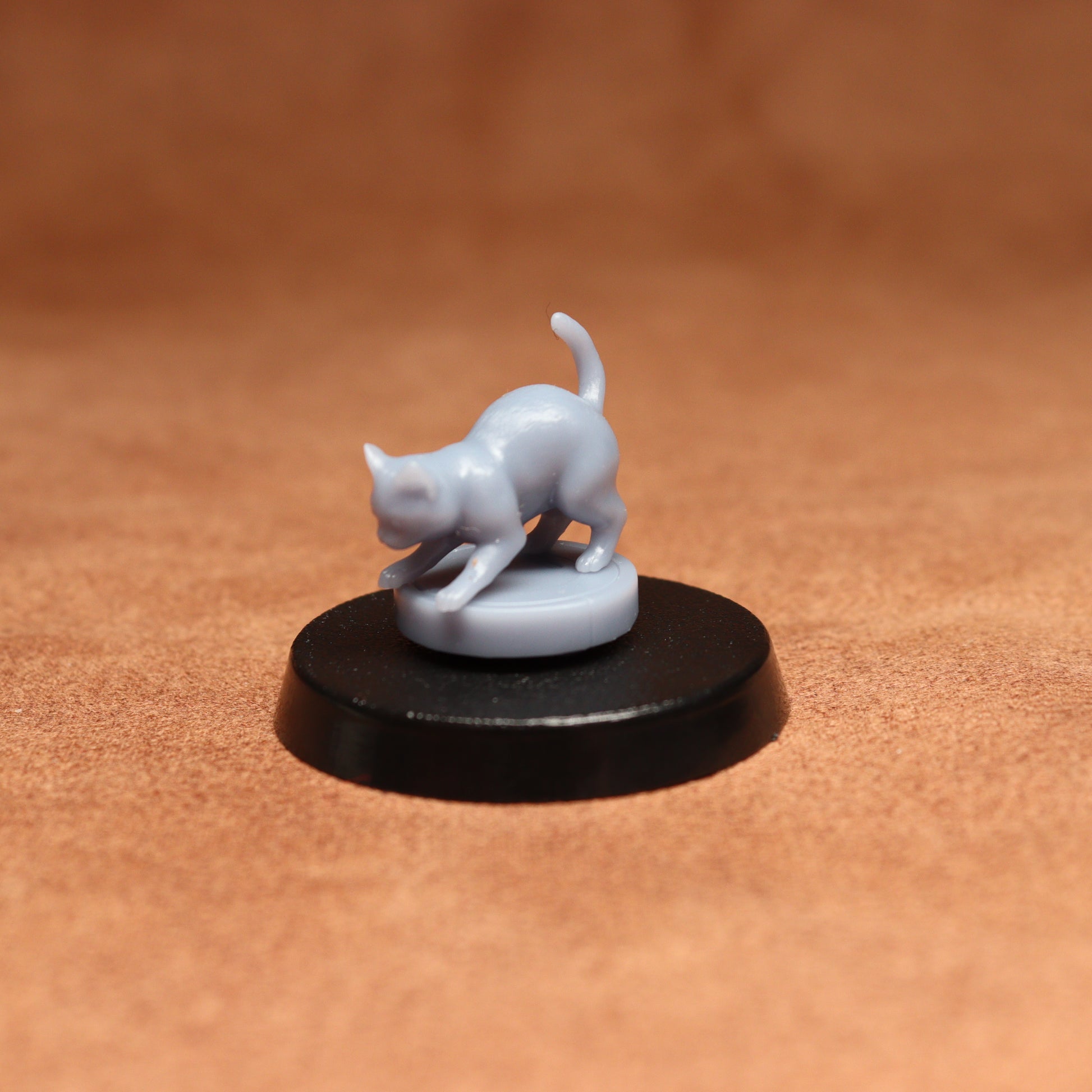 grey resin miniature cat figure on a black base with a brown background