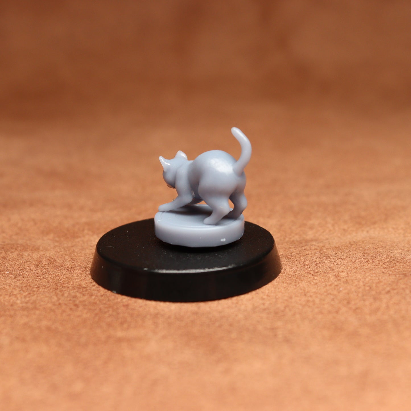 grey resin miniature cat figure on a black base with a brown background