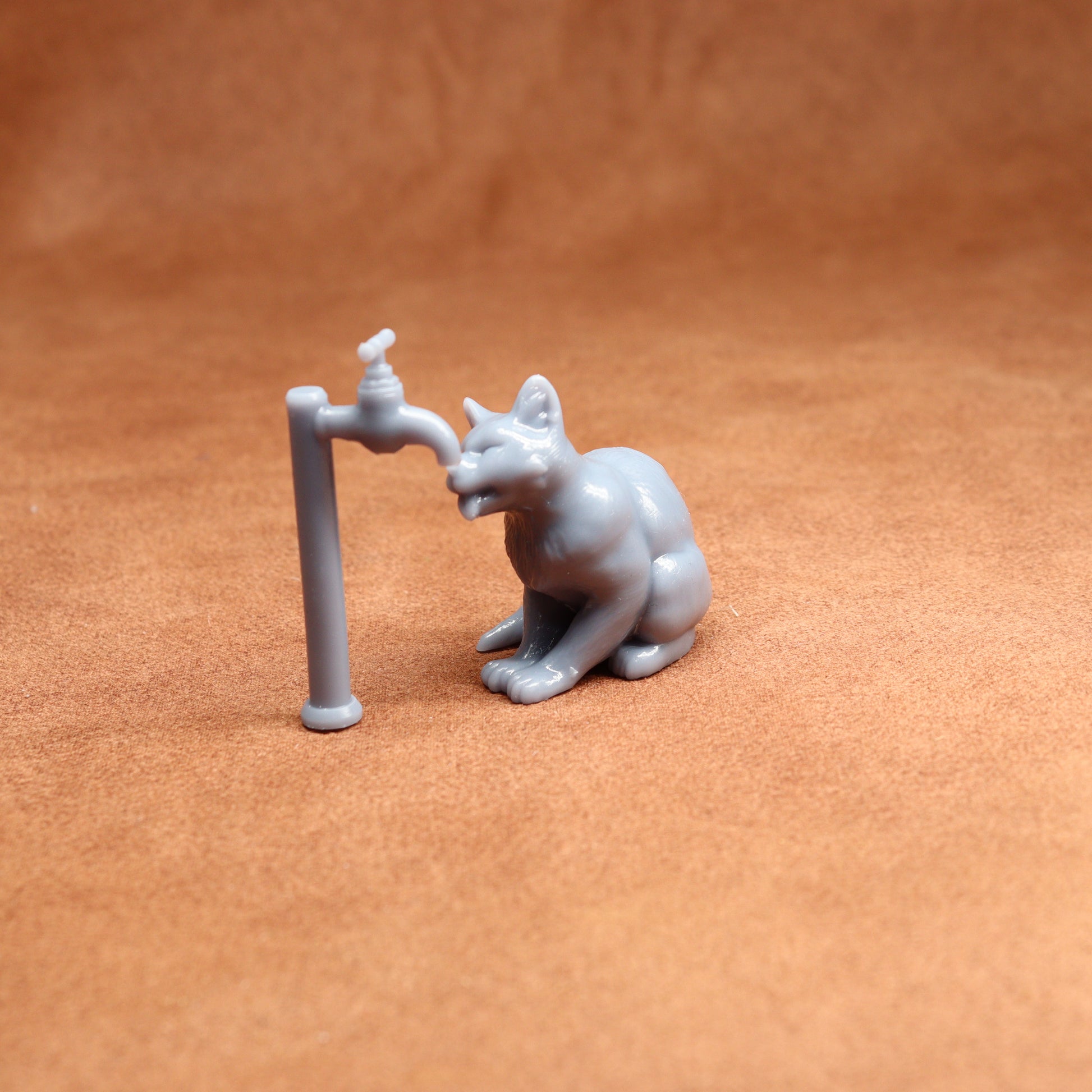 Small figurine of a cat interacting with a tap on a brown surface