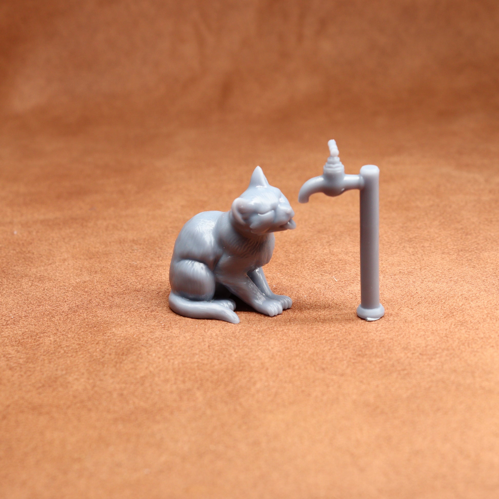 Small figurine of a cat interacting with a tap on a brown surface