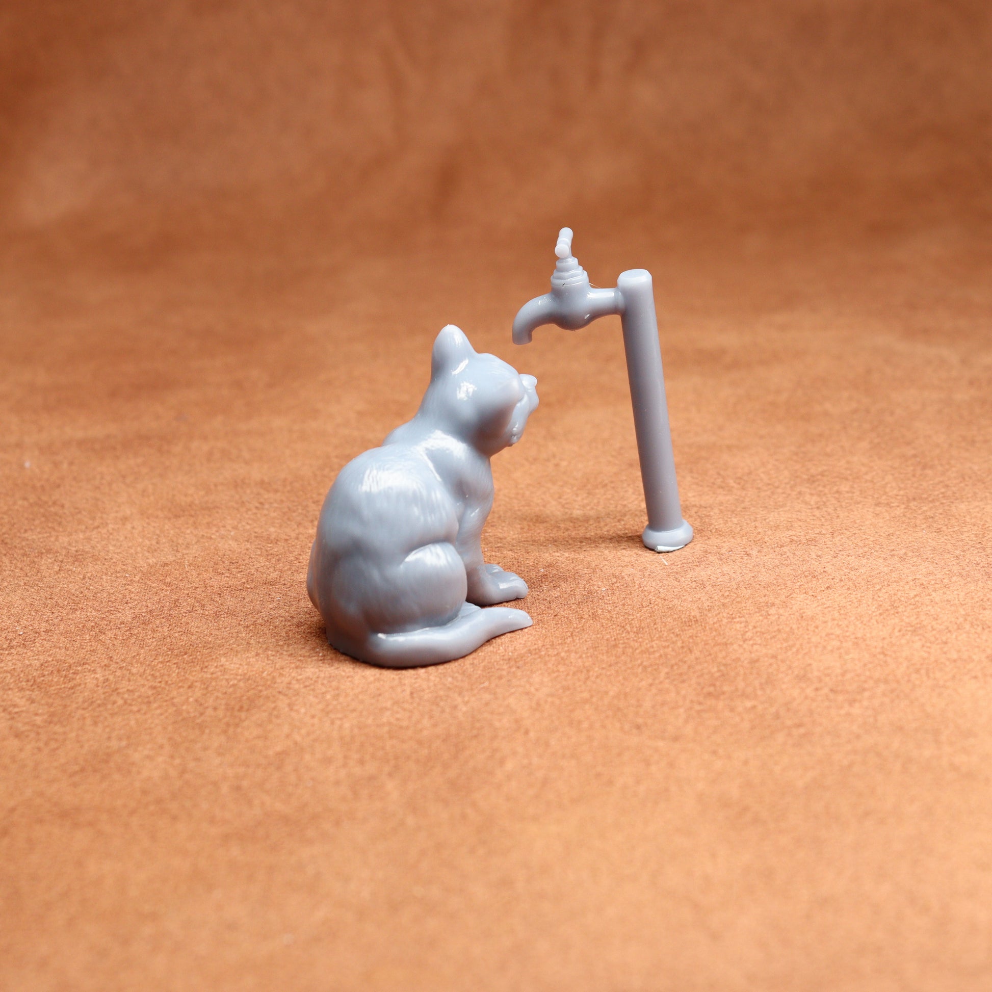 Small figurine of a cat interacting with a tap on a brown surface