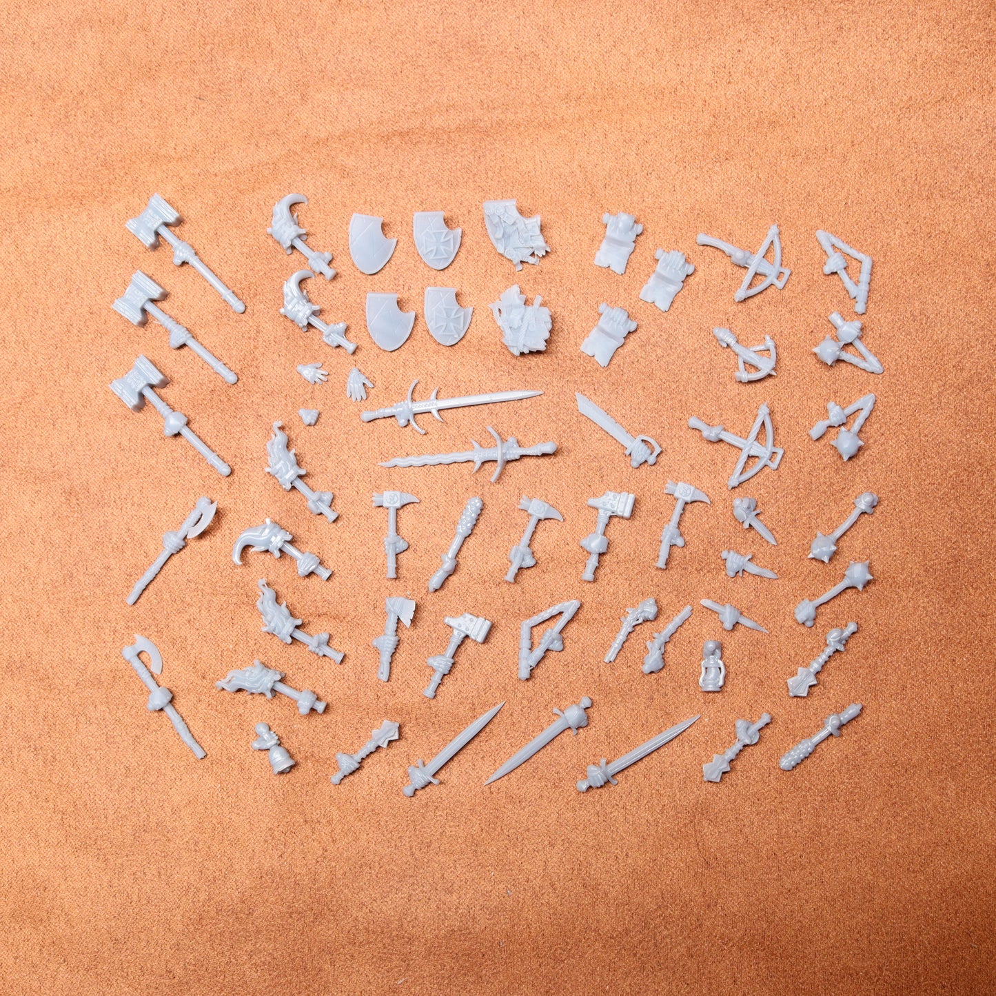 Collection of white resin toy figures and weapons on a brown surface