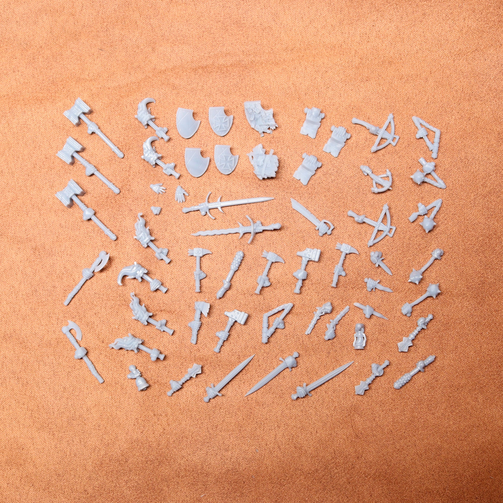 Collection of white resin toy figures and weapons on a brown surface