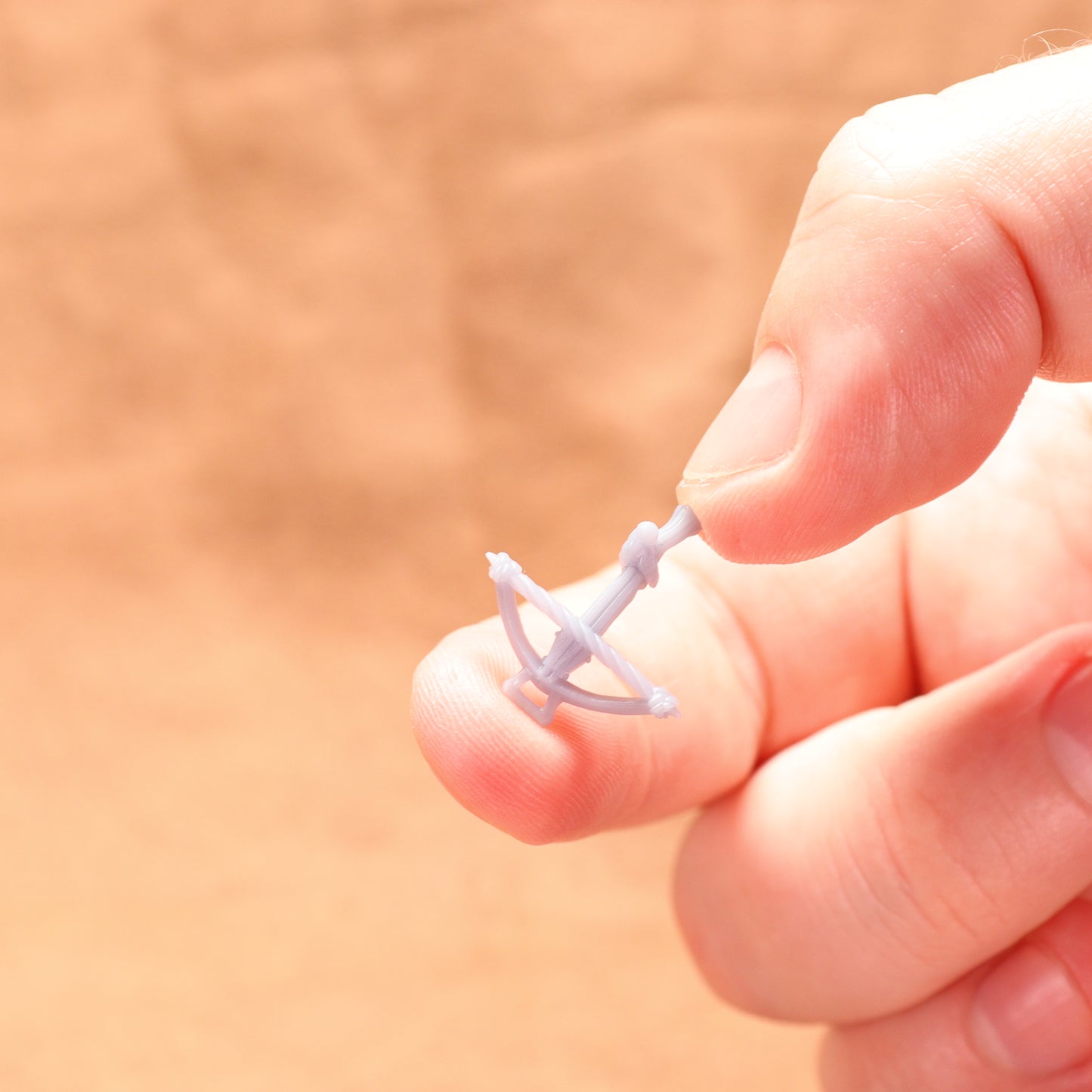 Small white archery bow held between fingers against a blurred background