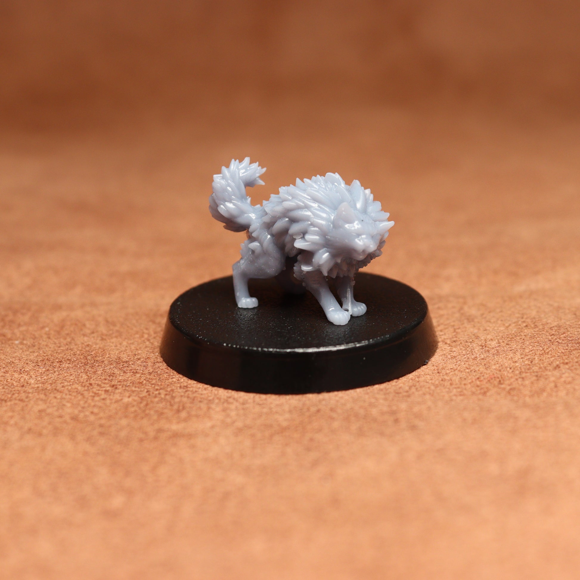 grey cat resin miniature on a black base on a brown background.