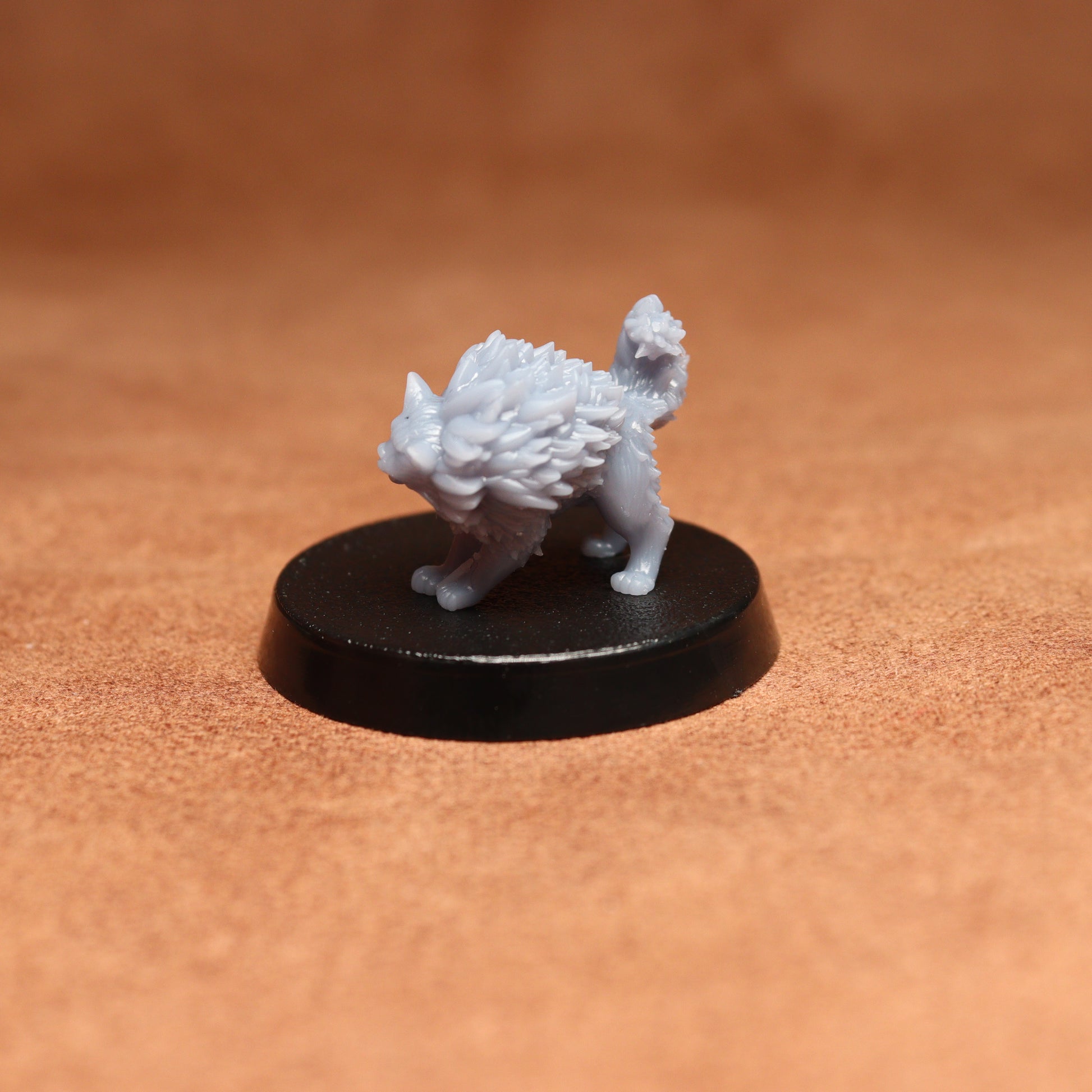 grey cat resin miniature on a black base on a brown background.