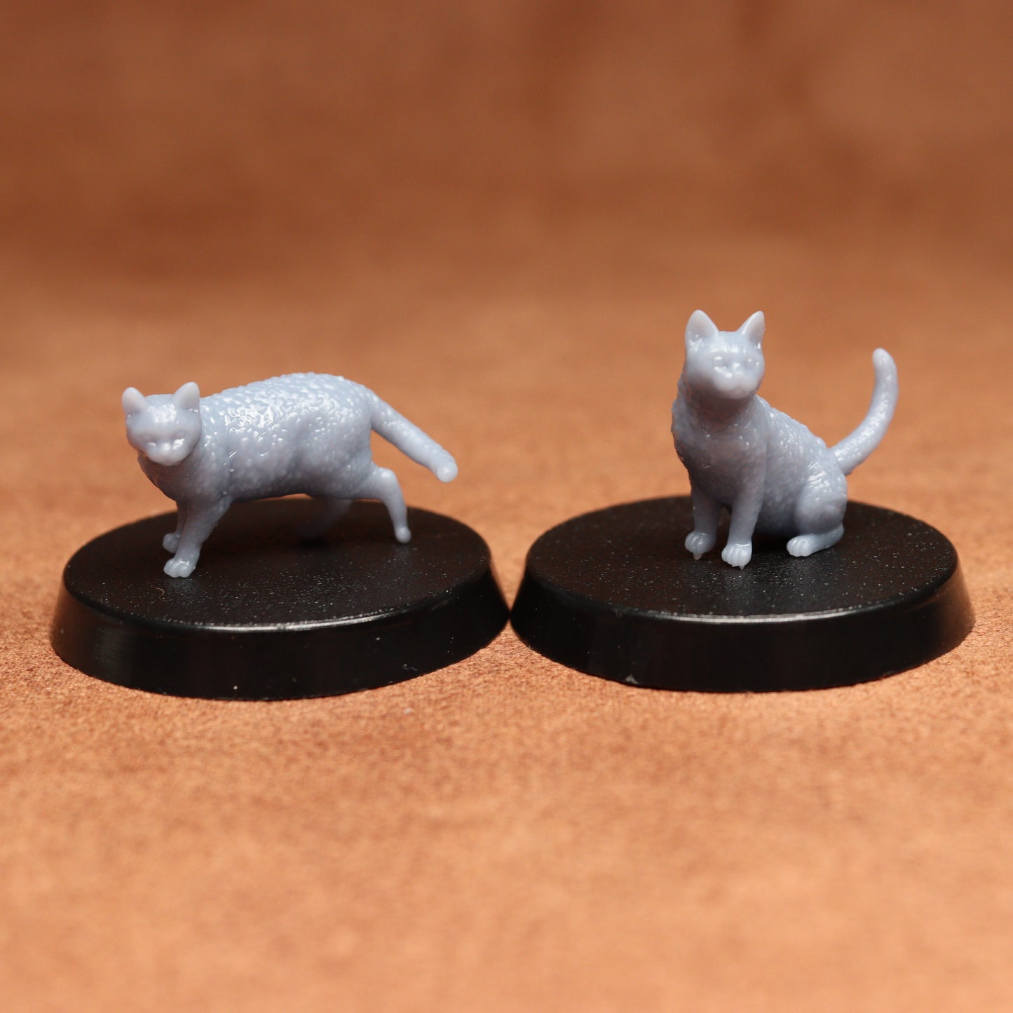 Two miniature cat figurines on black bases against a brown background