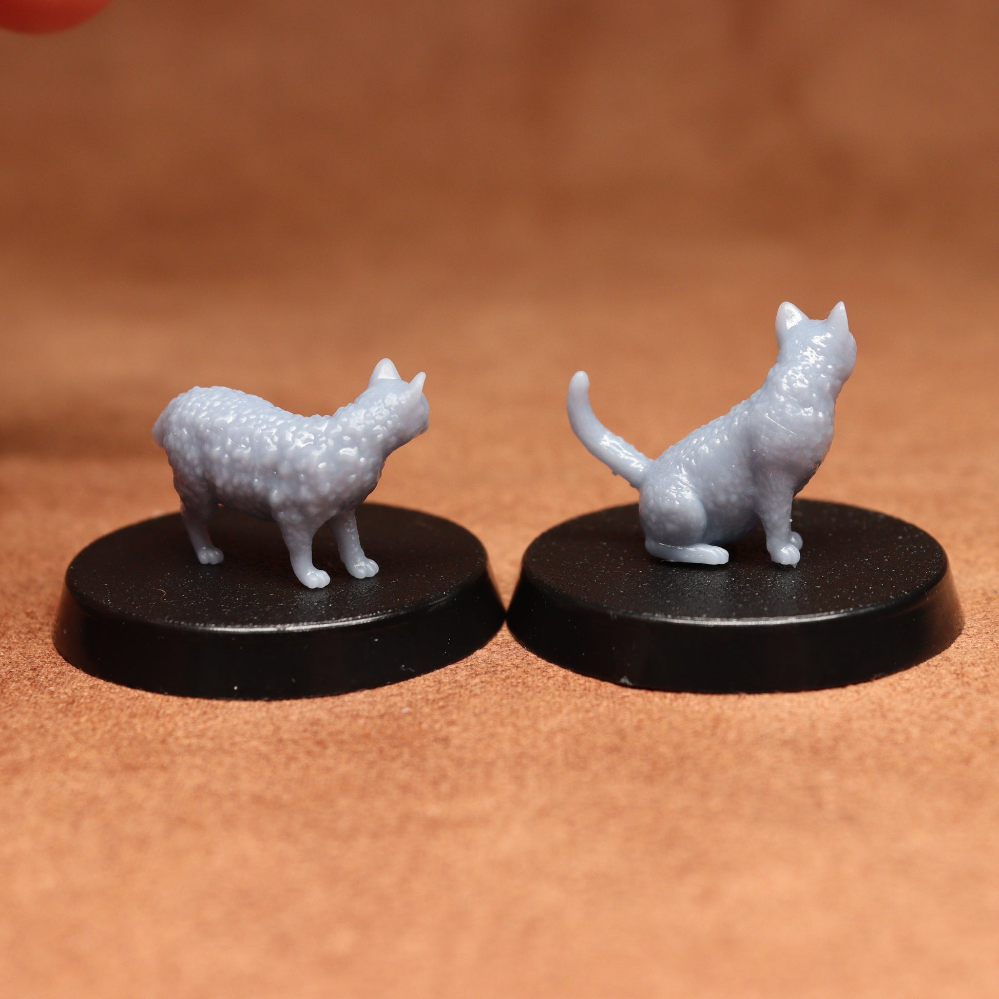Two miniature cat figurines on black bases against a brown background