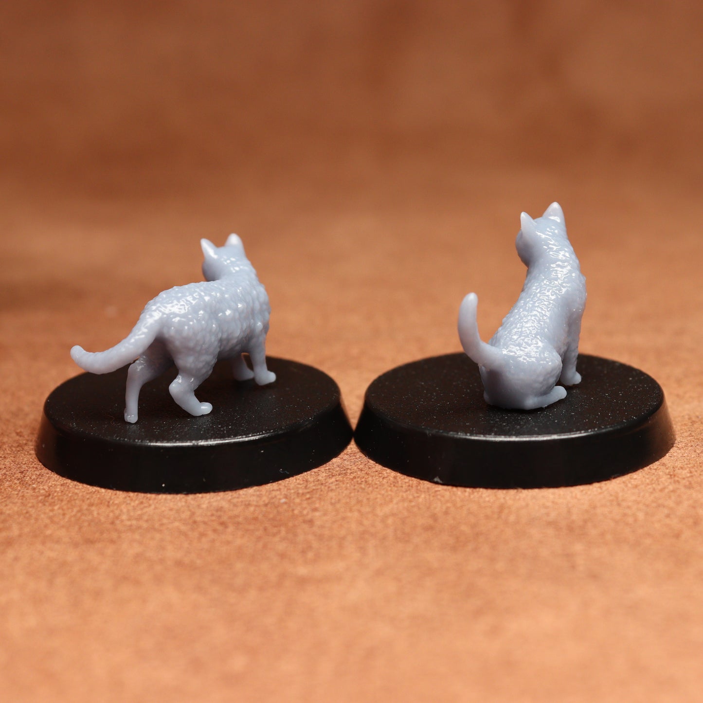 Two miniature cat figurines on black bases against a brown background