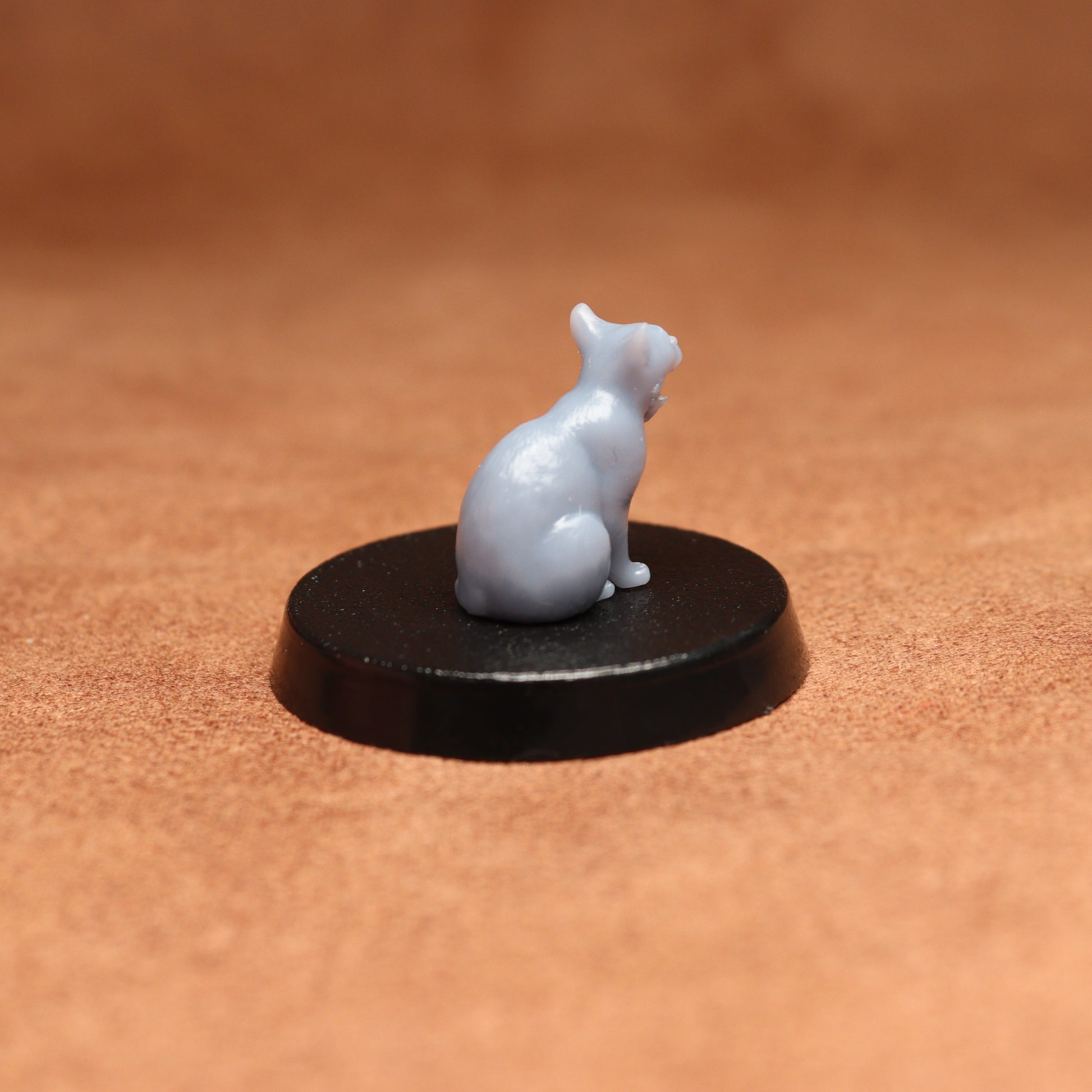 grey cat resin miniature on a black base on a brown background.