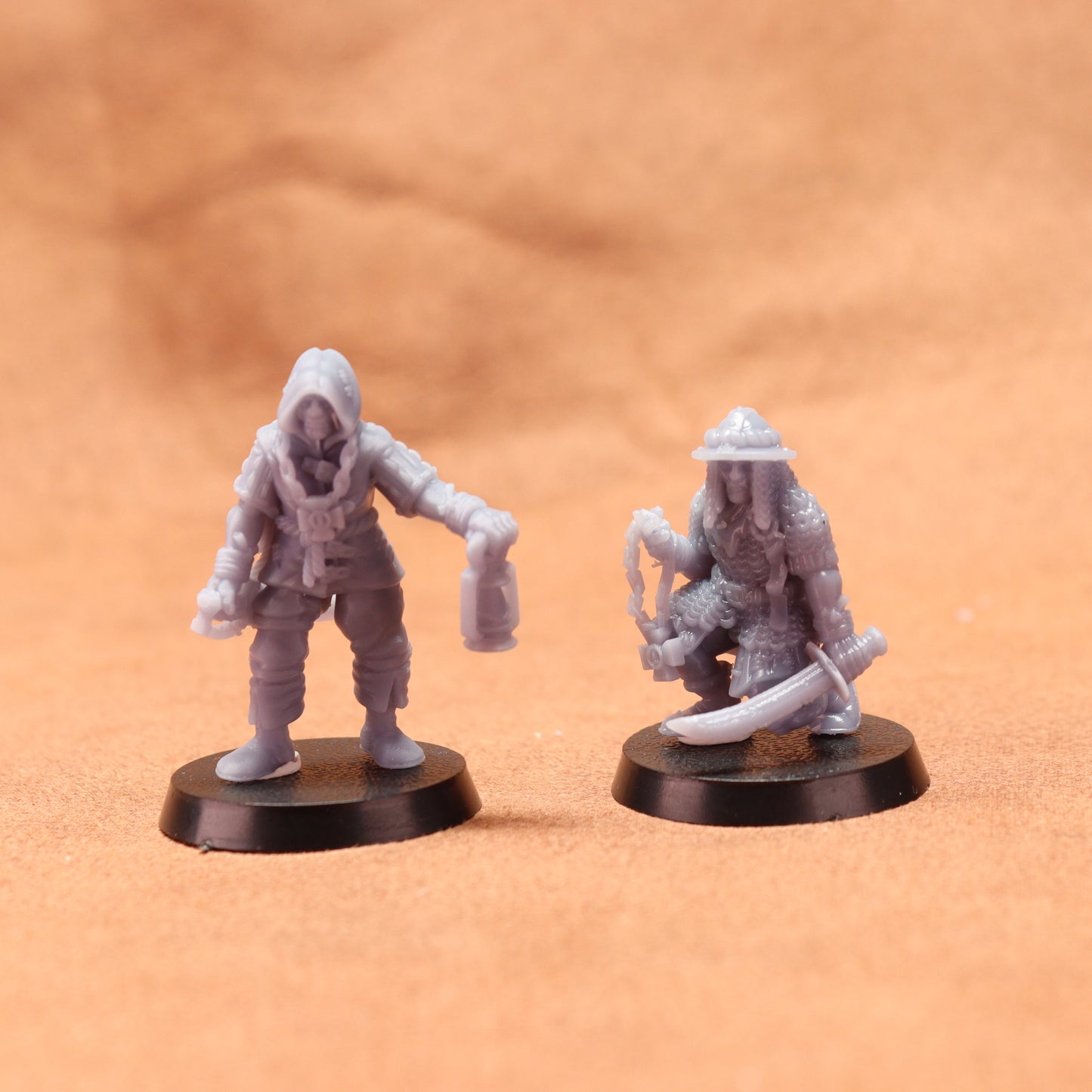 Two miniature figures on round bases against a brown background