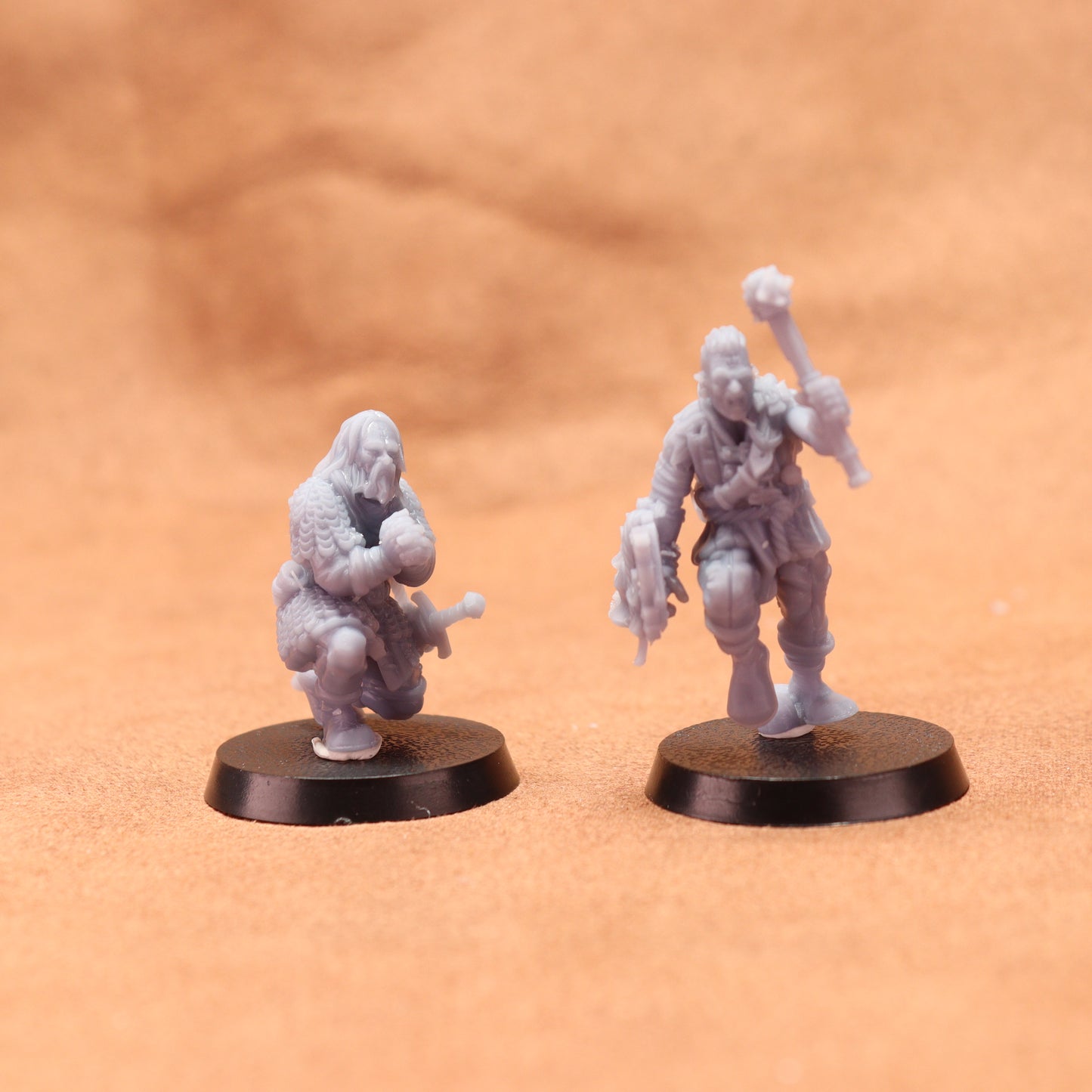 Two miniature figures on round bases against a brown background
